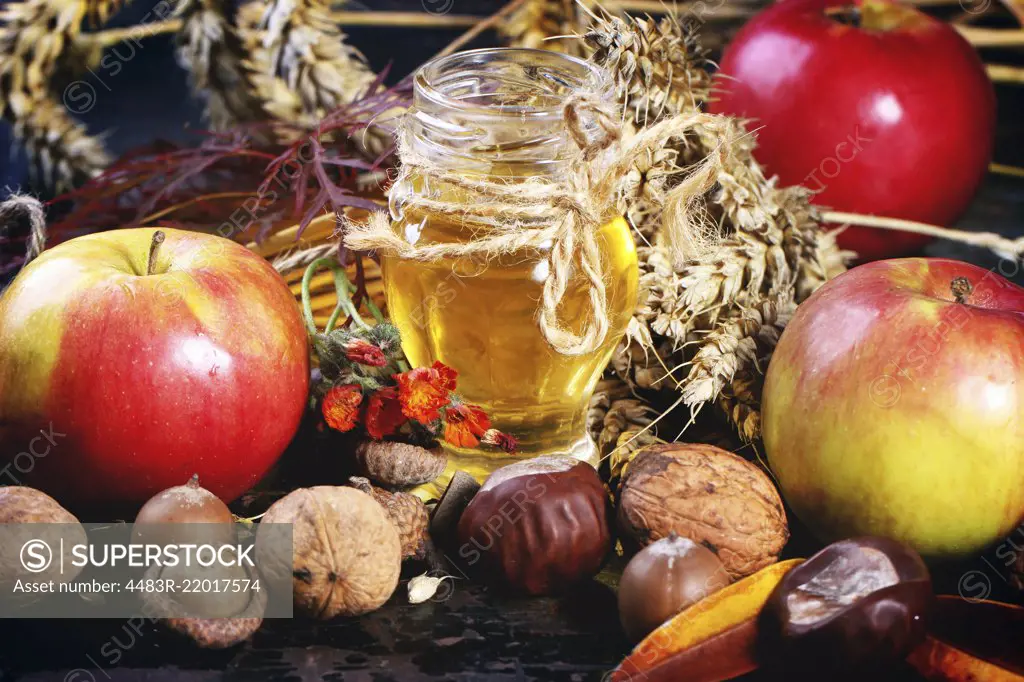 Glass jar of honey with apples, ears of wheat, chestnuts and walnuts over black wooden table