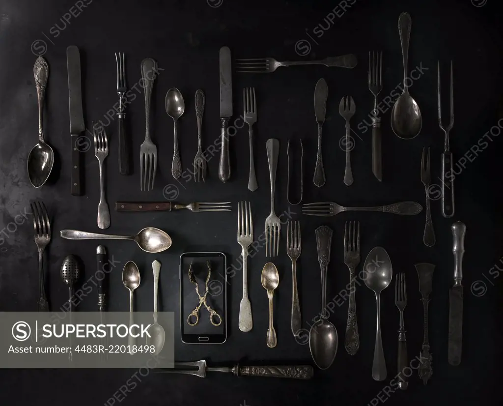 Big set of vintage cutlery with smartphote over black metal background. Top view