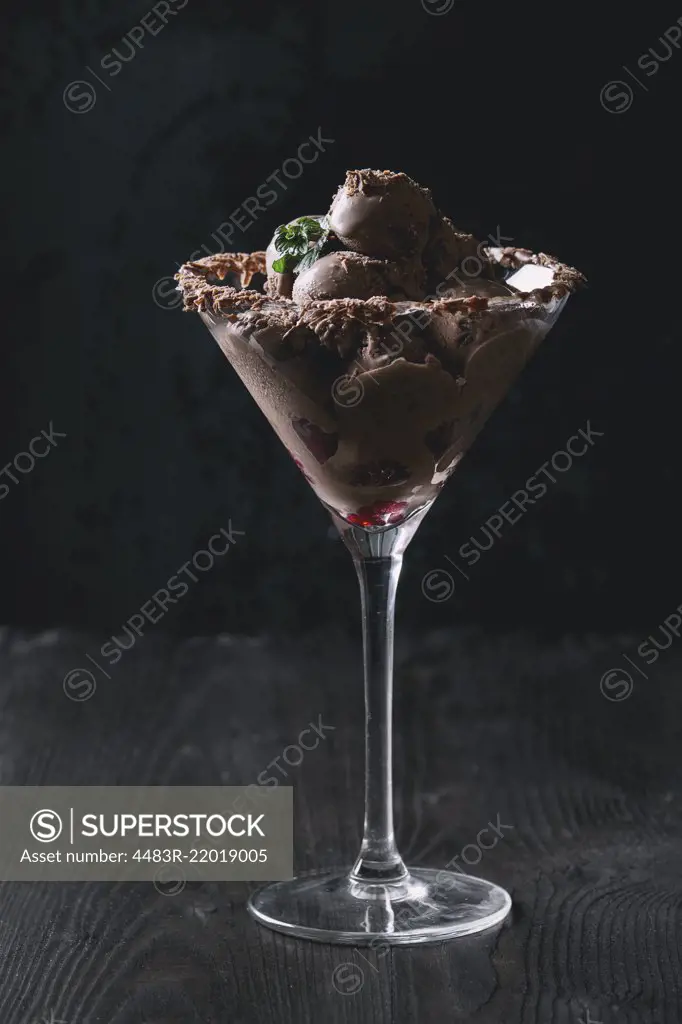 Cocktail glass with chocolate ice cream mini balls with fresh raspberries and mint on black burnt wooden background. Dark toned image