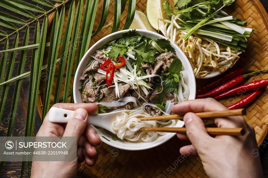 Pho Bo Soup with beef and chopsticks in male hands close-up