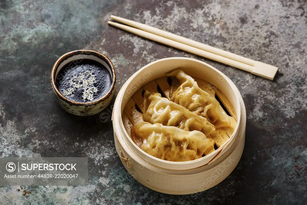 Steamed dumplings Gyoza in bamboo steamer with chopsticks and sauce on metal background