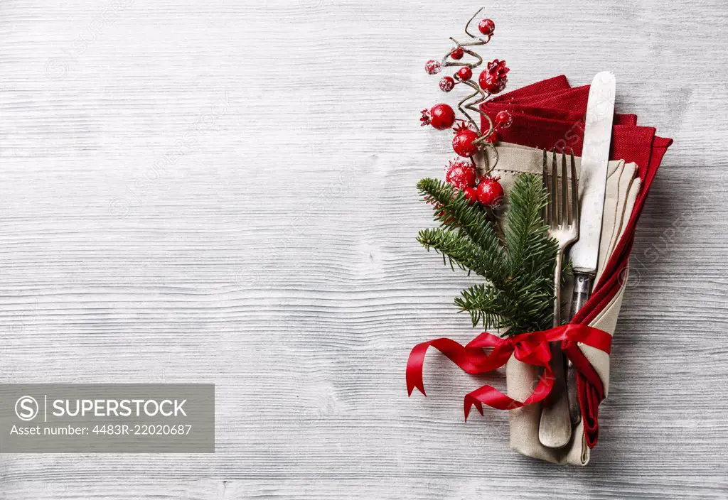 Table fork and knife set with napkin, christmas fir branch, red berries and ribbon on gray wooden background copy space