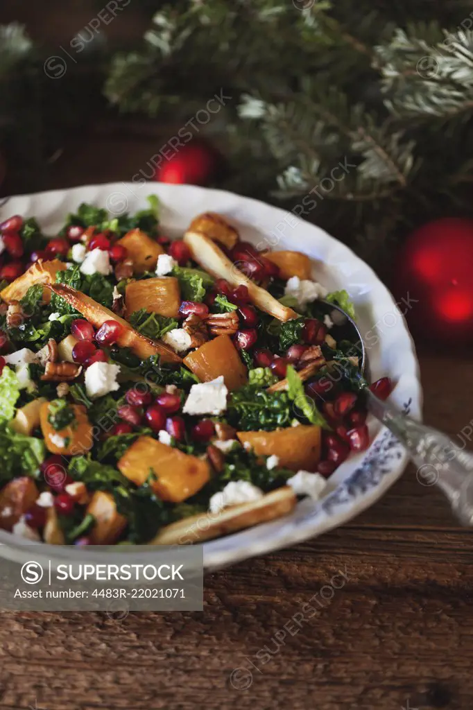 Festive kale, roasted sweet potatoes and parsnips salad with Feta cheese, pecans and pomegranate in a bowl