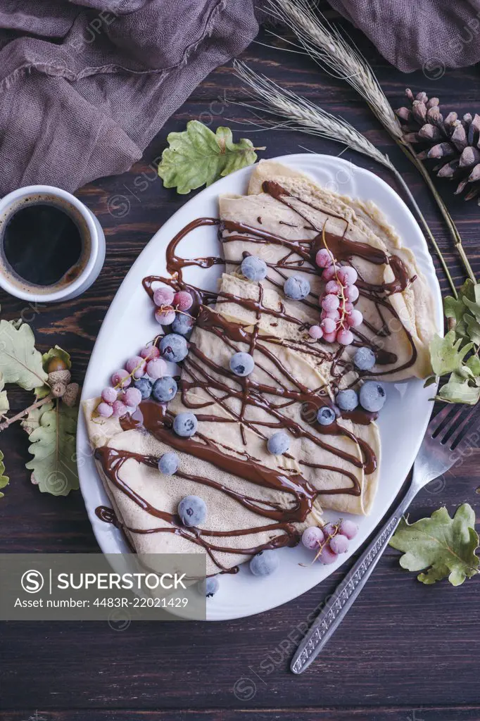 Crepes with chocolate drizzle and frozen berries and cup of black coffee