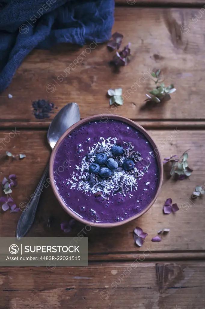 Blueberry acai smoothie bowl topped with blueberries, shredded coconut and cacao nibs on rustic wooden table