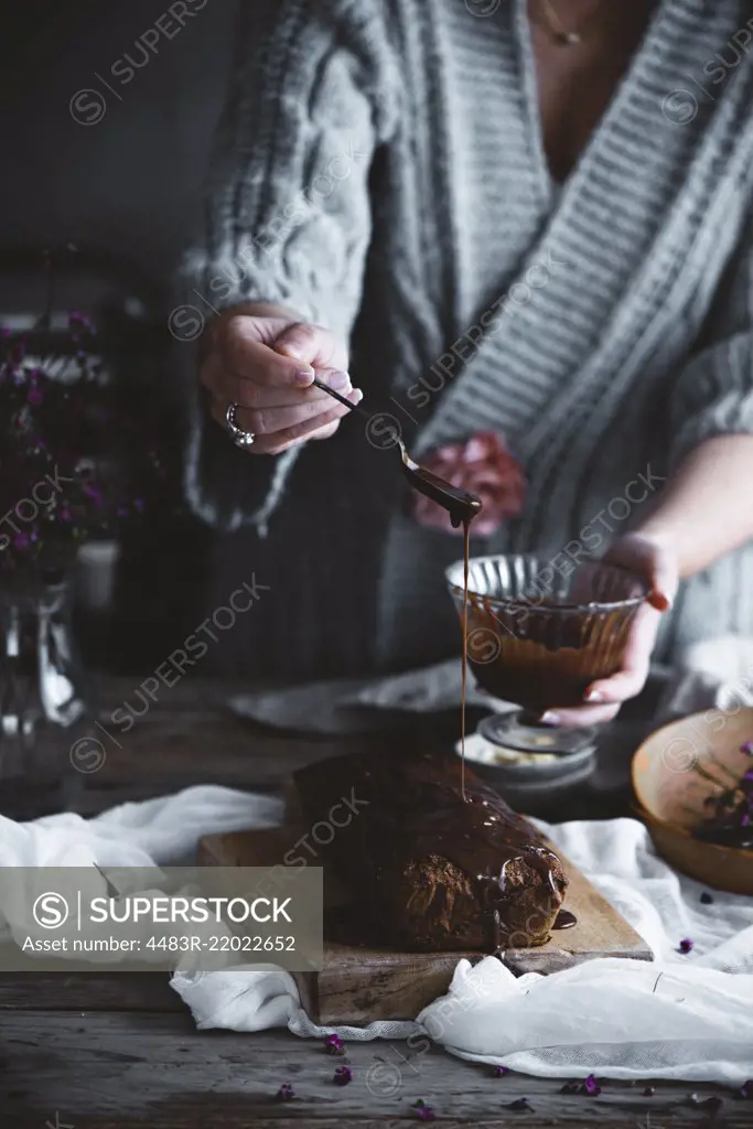 A woman pouring chocolate icing over a cake in a country kitchen