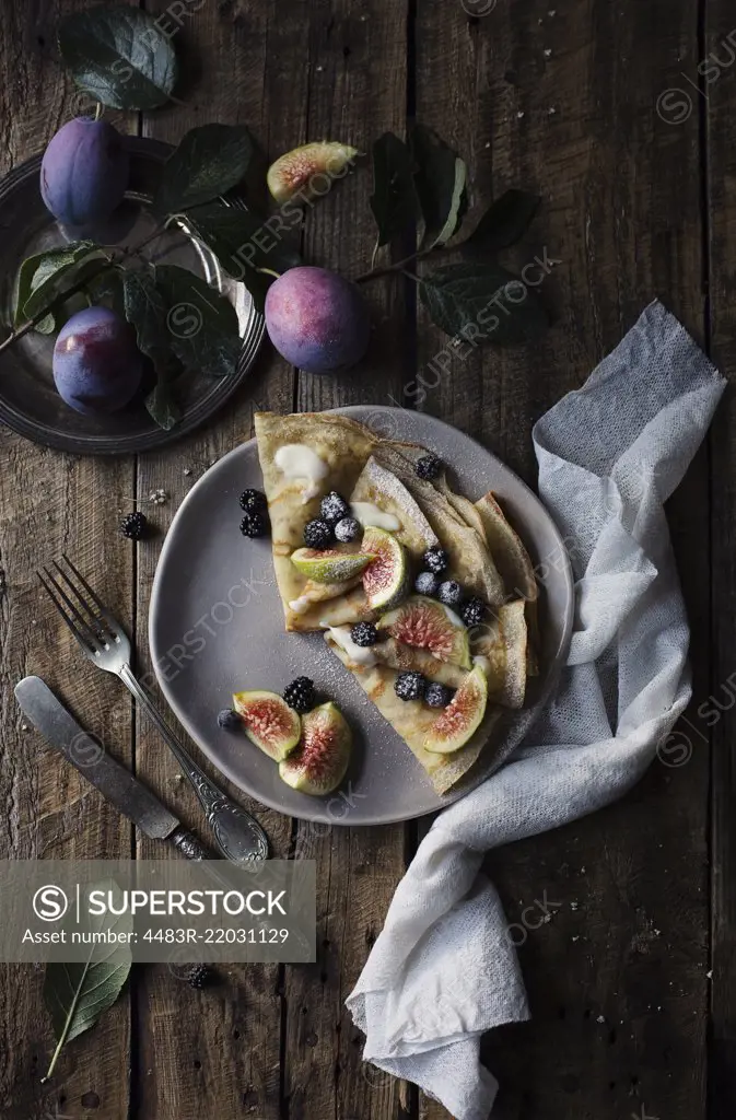 Crepes with figs and blackberries on wooden table. Top view