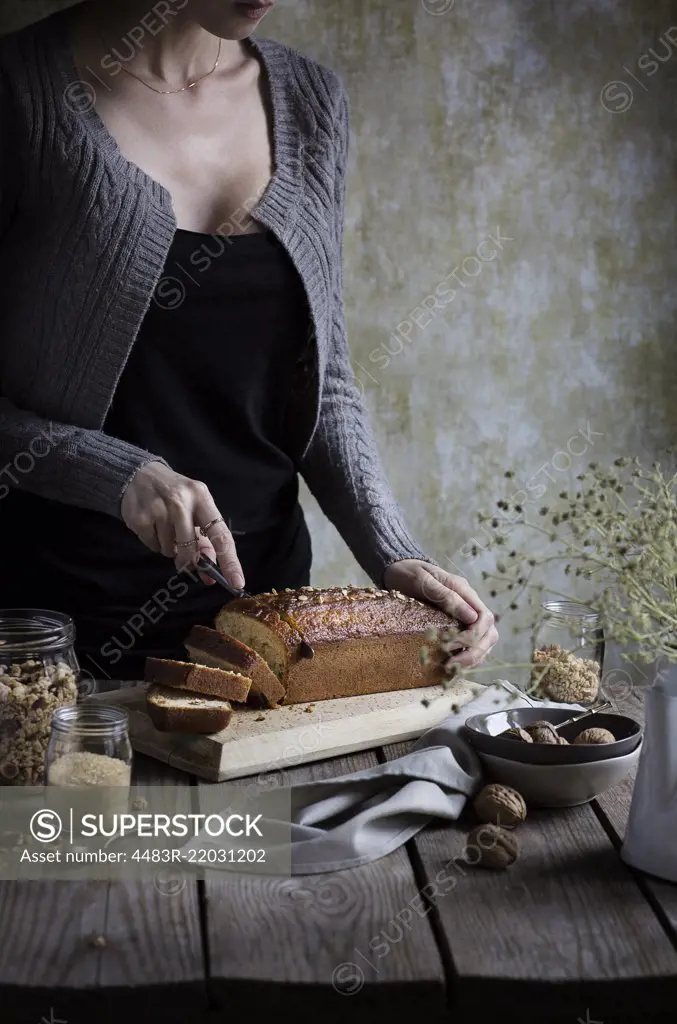 Woman cutting muesli cake on a rustic wooden table