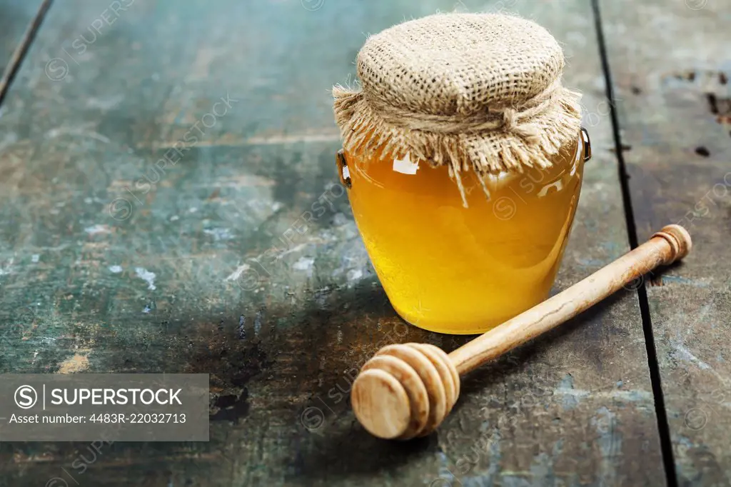 Honey jar and dipper on wooden background