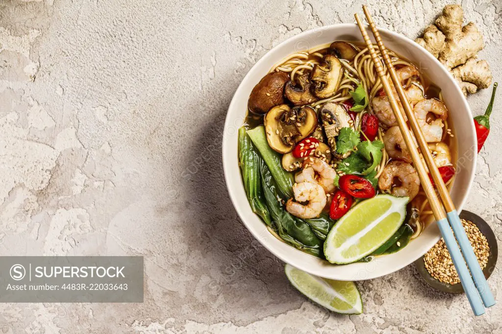 Asian soup with noodles (ramen), with miso paste, soy sauce, greens, mushrooms and shrimps prawn. On a stone table, with chopsticks, ginger and lime