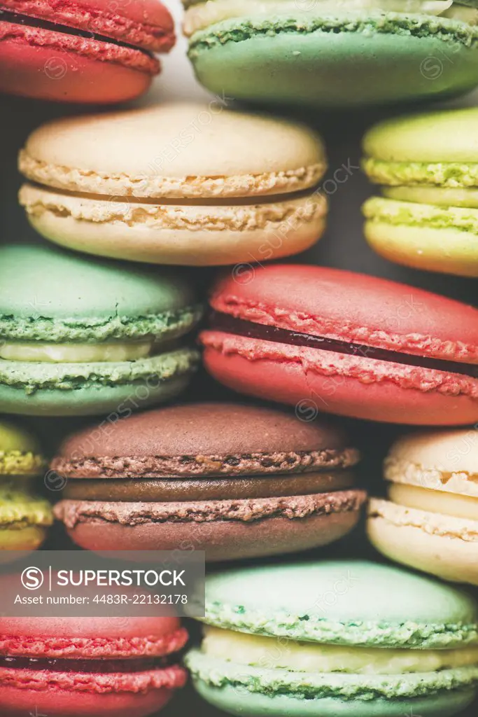 Flat-lay of sweet colorful French macaroon cookies stacked in rows, top view, vertical composition