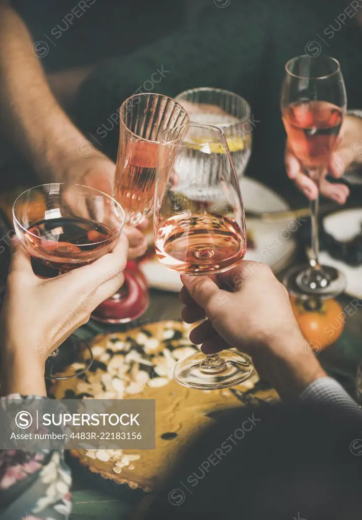 Traditional Christmas or New Year holiday celebration party. Friends or family feasting and clinking glasses with rose wine at festive Christmas table with homemade snacks, vertical composition