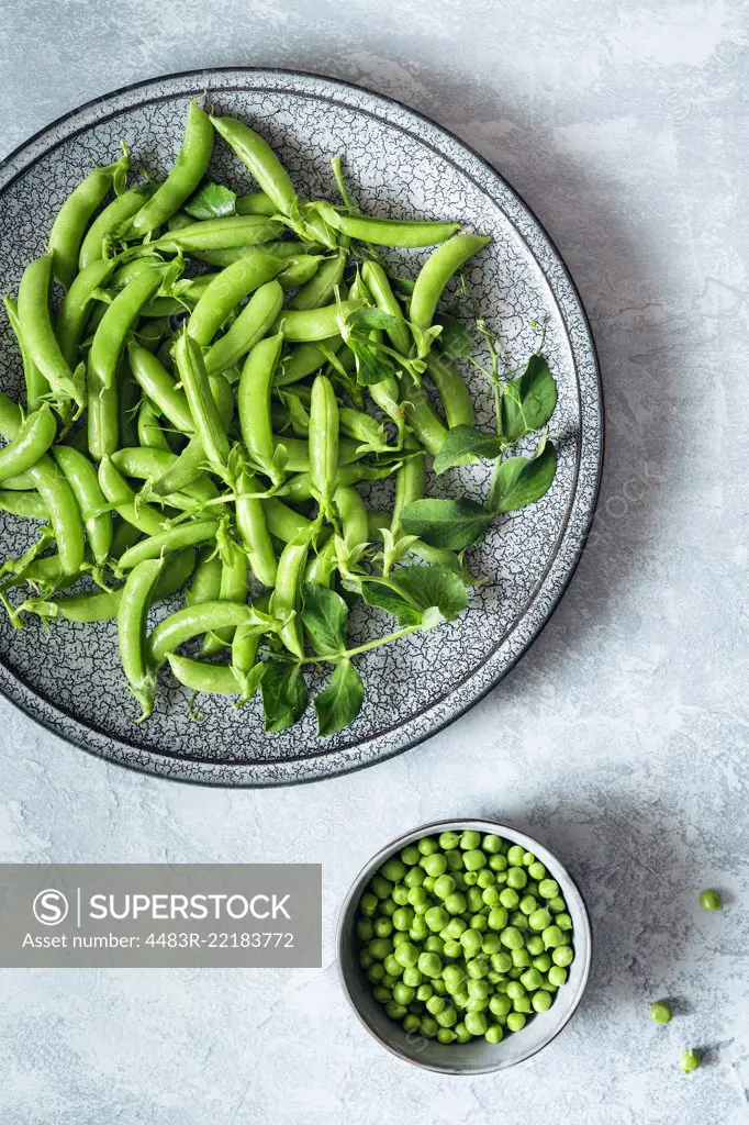 Green organic pea pods on a plate and shelled peas in a bowl.