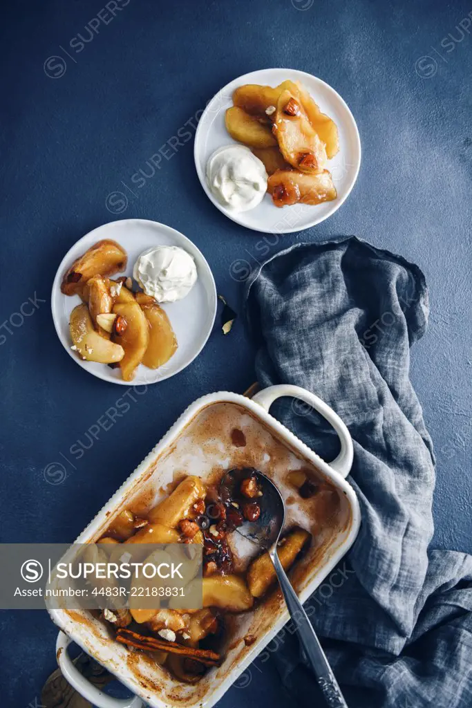 Cinnamon baked apple slices in a baking pan accompanied by two white plates with baked apple slices.