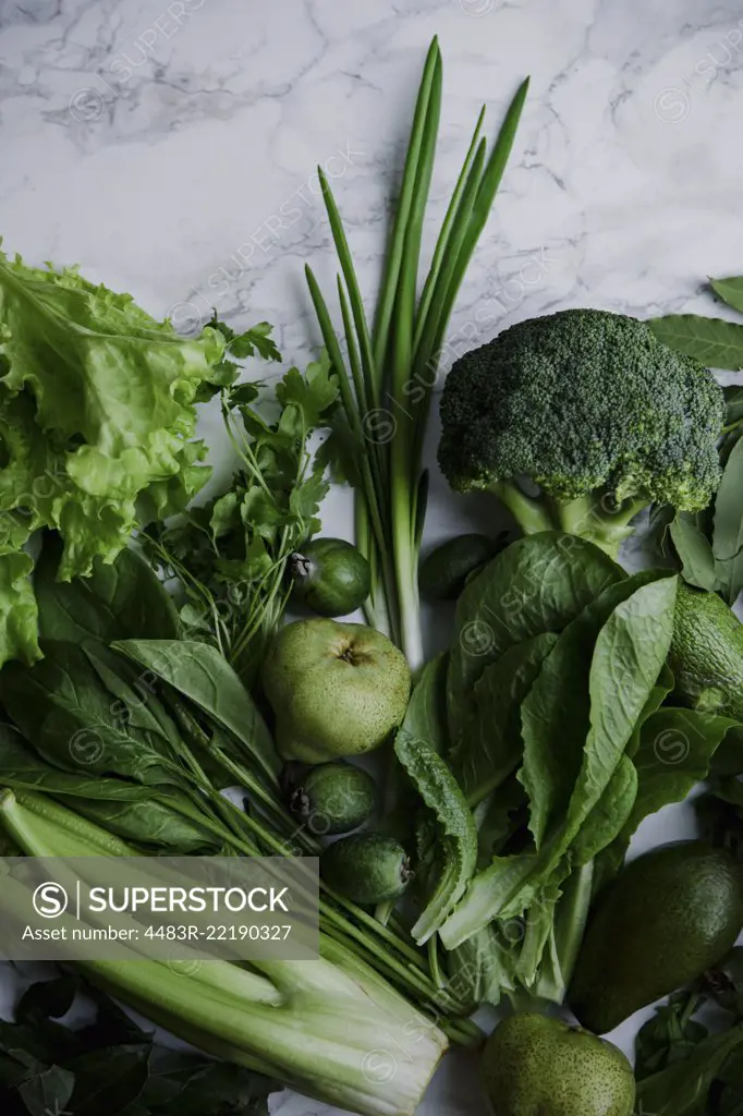 Fresh green food, variety of vegetables, greens and fruits on marble surface. Healthy eating concept. Monochromatic idea.