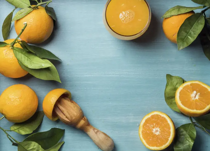 Fresh orange juice in glass and oranges with leaves on wooden turquoise blue painted background. Top view, copy space