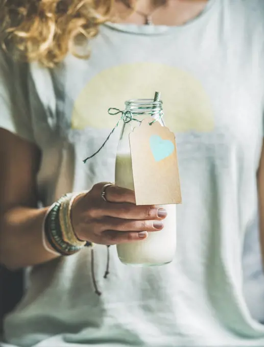 Young blond woman in grey light holding bottle of dairy-free almond milk in her hand. Clean eating, vegan, vegetarian, dieting, healthy food concept