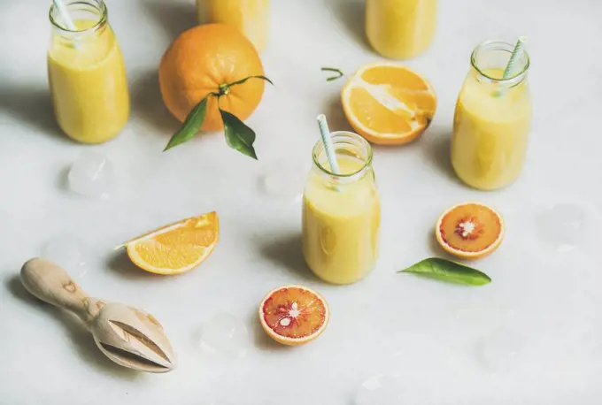 Healthy yellow smoothie with citrus fruit, ginger, ice in glass bottles over light marble table background, selective focus. Clean eating, vegan, vegetarian, detox, dieting food concept