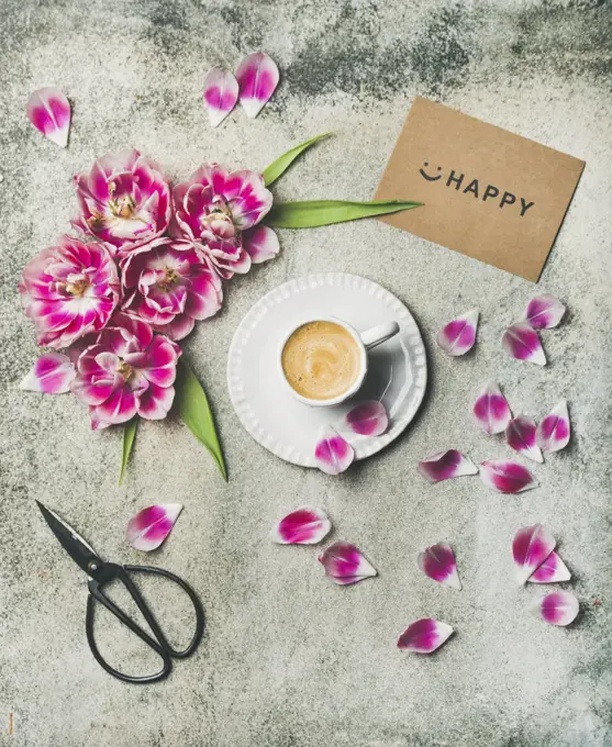 Spring morning concept. Flat-lay of cup of coffee surrounded with pink tulip flowers and sign happy over grey marble background, top view