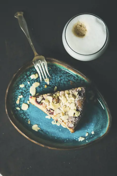 Dessert and coffee. Piece of lemon, ricotta, almond and raspberry gluten-free cake and glass of latte over dark wooden background, top view