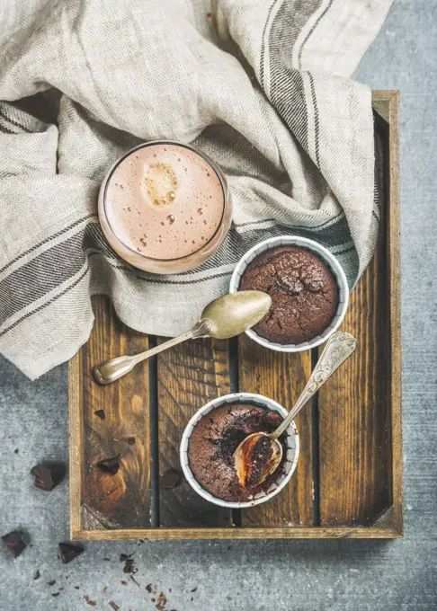 Chocolate souffle in blue individual baking cups and chocolate mocha coffee in wooden serving tray over grey concrete background, top view