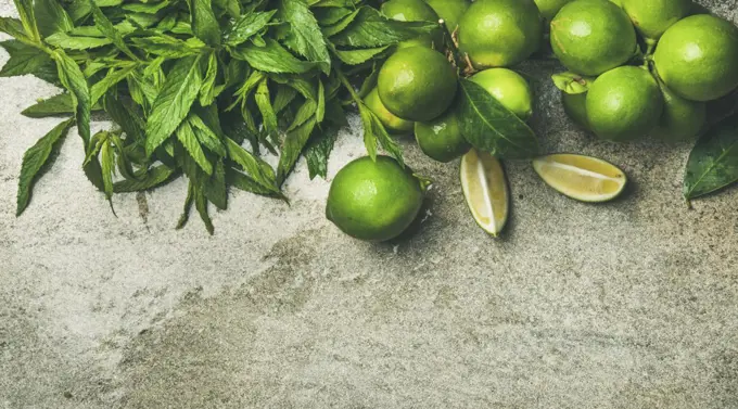 Flatlay of freshly picked organic limes and mint for making cocktail or lemonade over grey concrete stone background, top view, copy space, horizontal composition