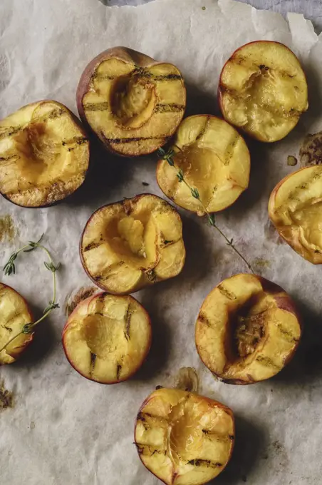 Grilled peaches and nectarines halved on baking paper sheet with thyme