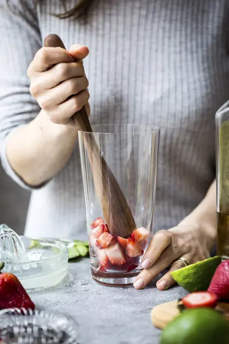 A woman is photographed as she is muddling strawberries to make margaritas.