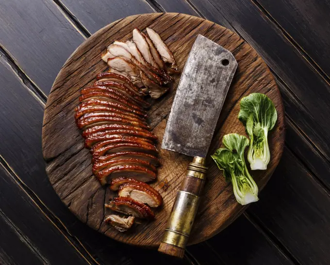 Sliced Peking Duck and cleaver on cutting board on black wooden background