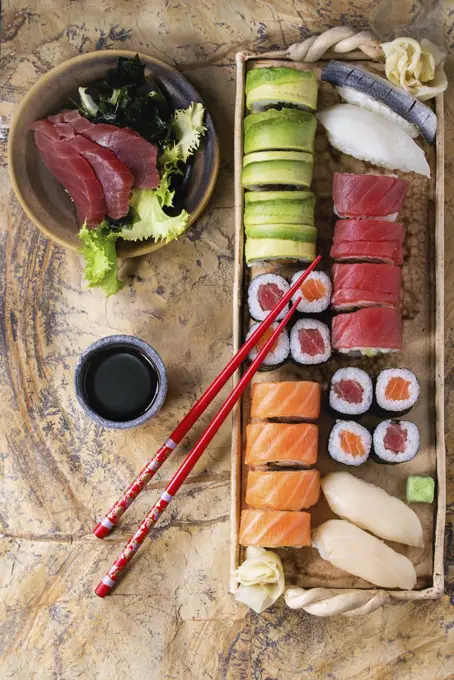 Sushi set nigiri, sashimi and rolls on clay plate served with chopsticks and soy sauce on stone surface. Flat lay.