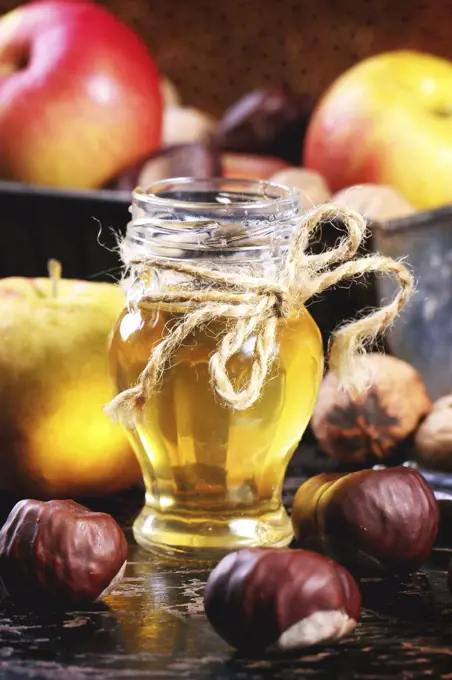 Glass jar of honey with apples, chestnuts and walnuts over black wooden table