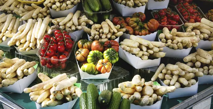 Market stall with fresh spring season vegetables at Parisian street farmers market. White asparagus, tomatoes, cucumbers.