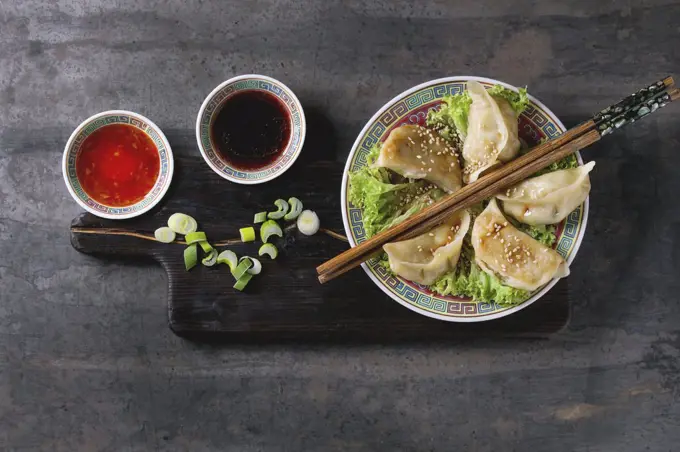 Gyozas potstickers on lettuce salad with sauces. Served in traditional china plate with chopsticks and spring onion on wood serving board over old metal background. Top view, space. Asian dinner