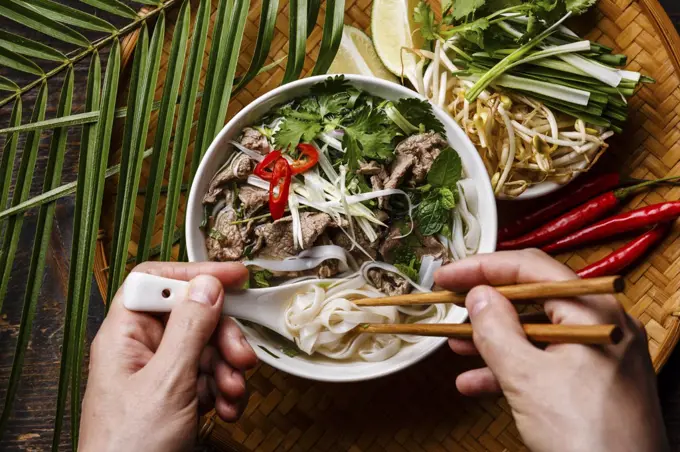 Pho Bo Soup with beef and chopsticks in male hands close-up