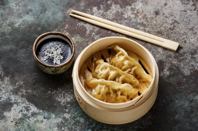 Steamed dumplings Gyoza in bamboo steamer with chopsticks and sauce on metal background