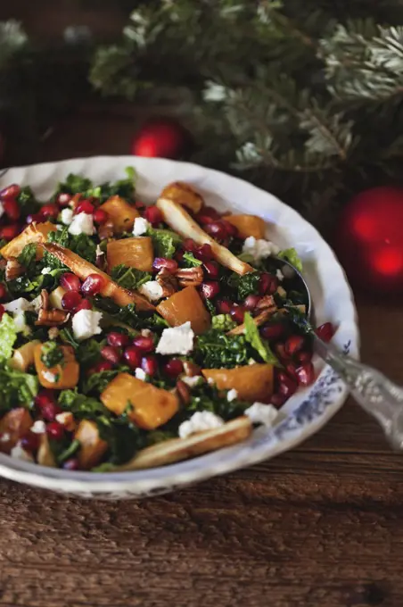 Festive kale, roasted sweet potatoes and parsnips salad with Feta cheese, pecans and pomegranate in a bowl