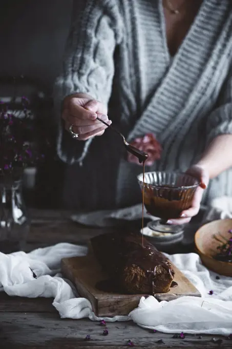 A woman pouring chocolate icing over a cake in a country kitchen