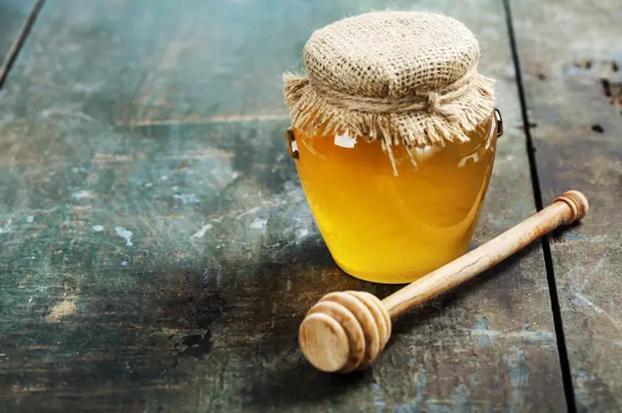 Honey jar and dipper on wooden background