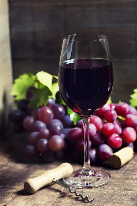 Red wine and red grapes on wooden background.