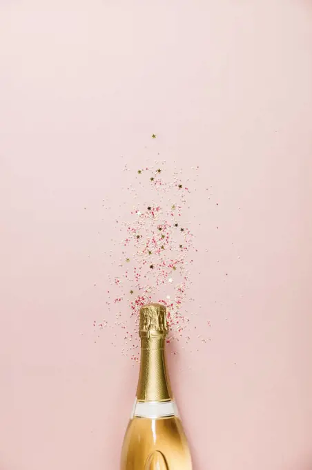 Flat lay of Celebration. Champagne bottle with ice cream sprinkles and golden star sprinkles on pink background. Top view