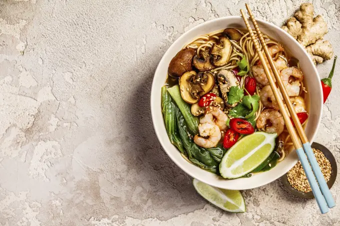 Asian soup with noodles (ramen), with miso paste, soy sauce, greens, mushrooms and shrimps prawn. On a stone table, with chopsticks, ginger and lime