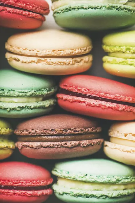 Flat-lay of sweet colorful French macaroon cookies stacked in rows, top view, vertical composition