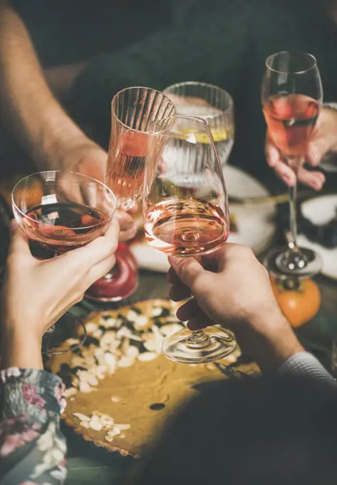 Traditional Christmas or New Year holiday celebration party. Friends or family feasting and clinking glasses with rose wine at festive Christmas table with homemade snacks, vertical composition