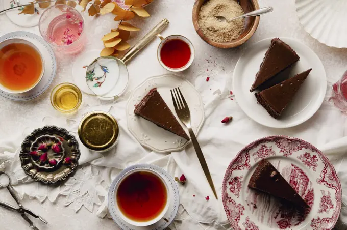 Overhead image of tea party with chocolate cheesecake slices on various plates. Traditional style, vintage tablecloth and cutlery.