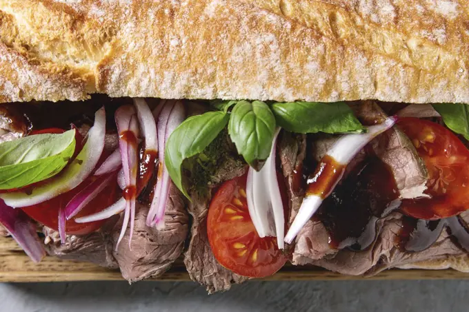 Close up of beef baguette sandwich with tomatoes, basil, red onion. Flat lay, space