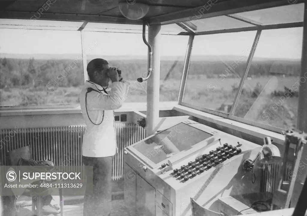 Air traffic controller in the 1940s. An officer in the airport control tower is monitoring the runway with binoculars.