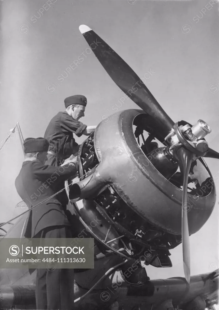 Airplane engineers.Three mechanics are performing the important last minute check of engine details before start. The airplane is a swedish single propeller engine light bomb and survaillance unit model B5. The swedish company Saab Svenska Aeroplan AB produced this airplane on license from American Northrop and their model 8A-1.  Picture taken in the 1940s during the second world war.