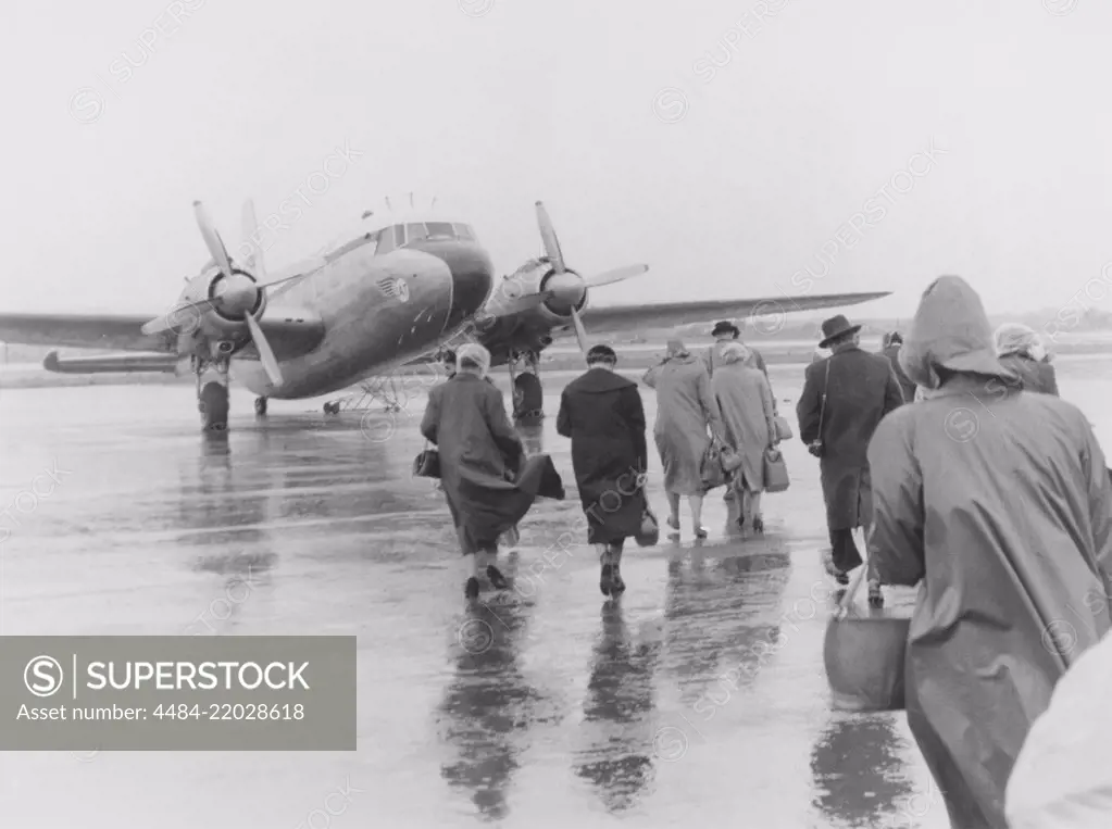 1950s vacation. A group of people are walking in the pouring rain towards the waiting plane bound for Spain. Sweden 1951. ref 385