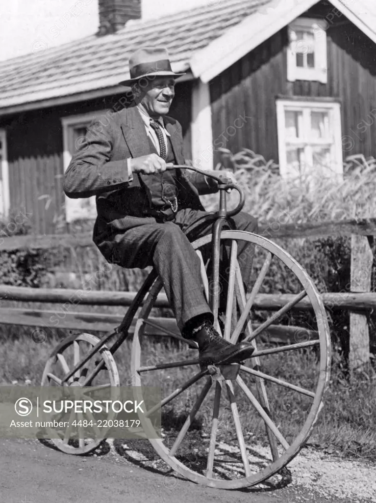 Penny farthing bicycle. A man is riding a penny-farthing bicycle he has made himself with wooden wheels both front and back. Sweden 1940s