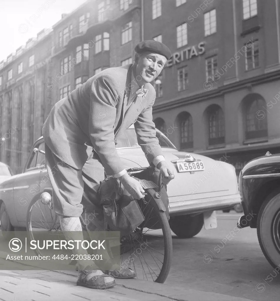 1950s man with his bicycle. A man in has parked his bicycle and balancing it on the kerb. He puts a chain around the back wheel, unabling it from being stolen. Notice the registration sign on the bicycle that was a mandatory item at this time. Sweden 1950s. Photo Kristoffersson ref BP57-5